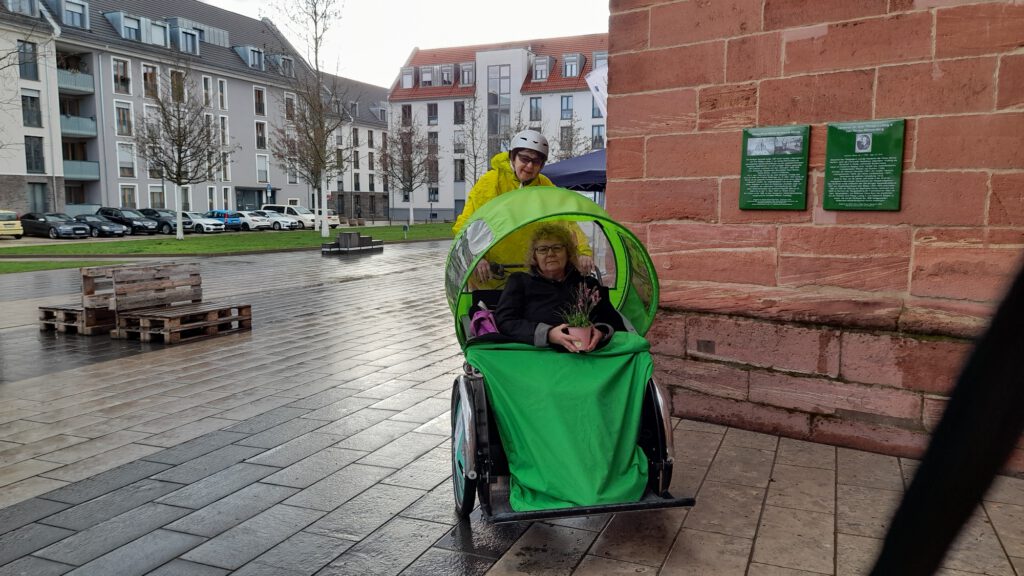 Eine Rikscha mit geschlossenem Regenverdeck steht auf einem nassen Platz vor einer Sandsteinmauer.