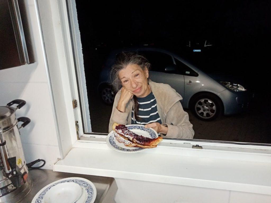 Eine Frau lehnt von außen in ein Fenster und hält den Teller mit dem Pfannkuchen in der Hand. Sie schaut verträumt.