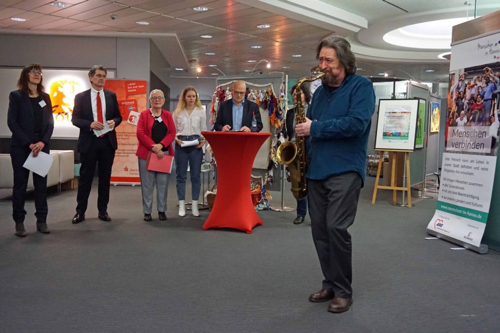 Saxophonist Daniel eröffnet die Ausstellung. Im Hintergrund sind die Organisatorinnen von Menschen in Hanau sowie Bürgermeister Weiss-Thiel zu sehen.