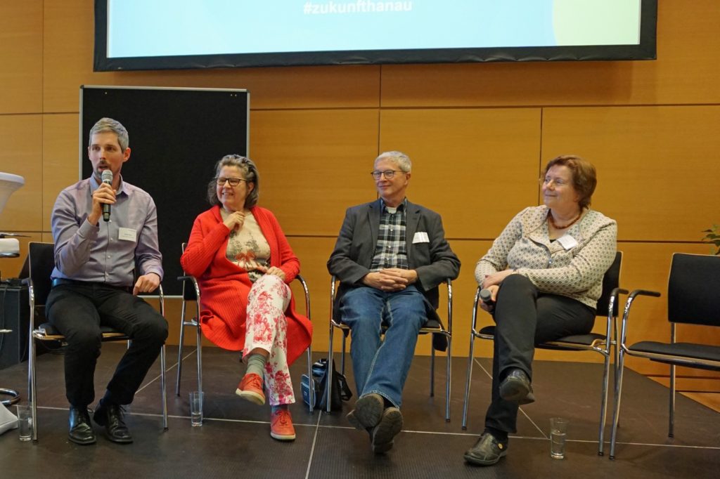 Foto von 4 Menschen auf Stühlen, beginnend mit Daniel mit Mikrophon, Beatrix in roter Kleidung, Calle von Hanau engagiert und Iris Fuchs, Leiterin der Hanauer Freiwilligenagentur.