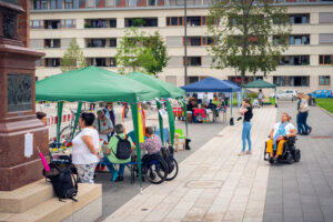 2021: Tauschmarkt mit mehreren Pavillions und Menschen auf dem Platz vor der Wallonisch-Niederländischen Kirche