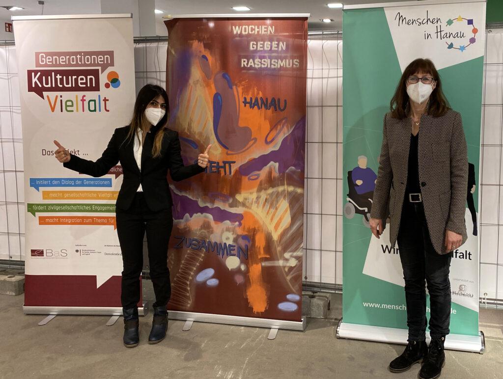 Resan, links, und Sylvie, rechts stehend, vor 3 Rollups zur den Internationalen Wochen gegen Rassismus