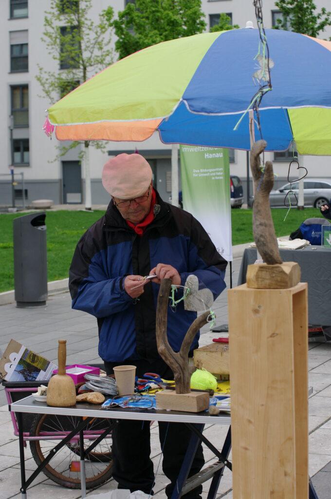 Ein Mann steht hinter einem kleinen Stand und präsentiert kleine Kunstwerke aus Holz.