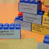 Übergroße Legosteine sind aufeinander gestapelt und mit Stichworten in verschiedenen Farben beklebt.