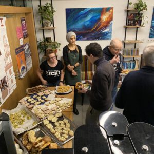 2024: Buffet beim Pub-Quiz. Auf einem Tisch stehen mehrere Platten mit Fingerfood. Mehrere Personen sind zu sehen, die davor stehen, manche essen.