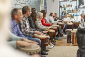 2024: Chancen-Patenschaften. Mehrere Personen trommeln auf Djembe-Trommeln.