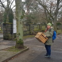 Eine dickbekleidete Frau trägt eine Kiste zum Sammeln der Blumenzwiebeln an den Friedhof.