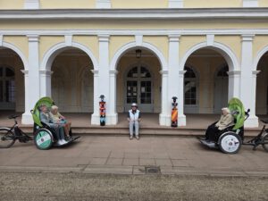 Zwei Rikschas mit Fahrgästen stehen vor den gelben Arkaden des Kurhauses in Wilhelmsbad.