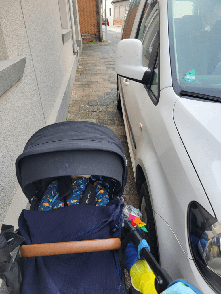 Ein Kinderwagen versucht an einem Auto vorbeizukommen.