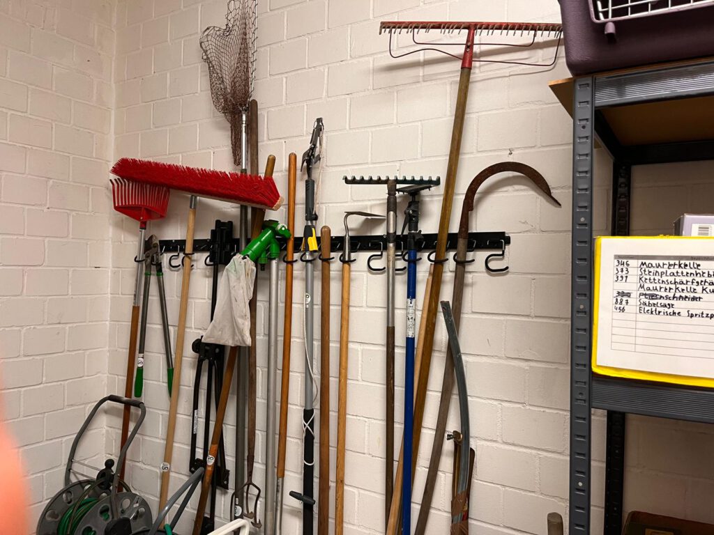 Auf mehreren Haken hängen Besen, Rechen und mehr