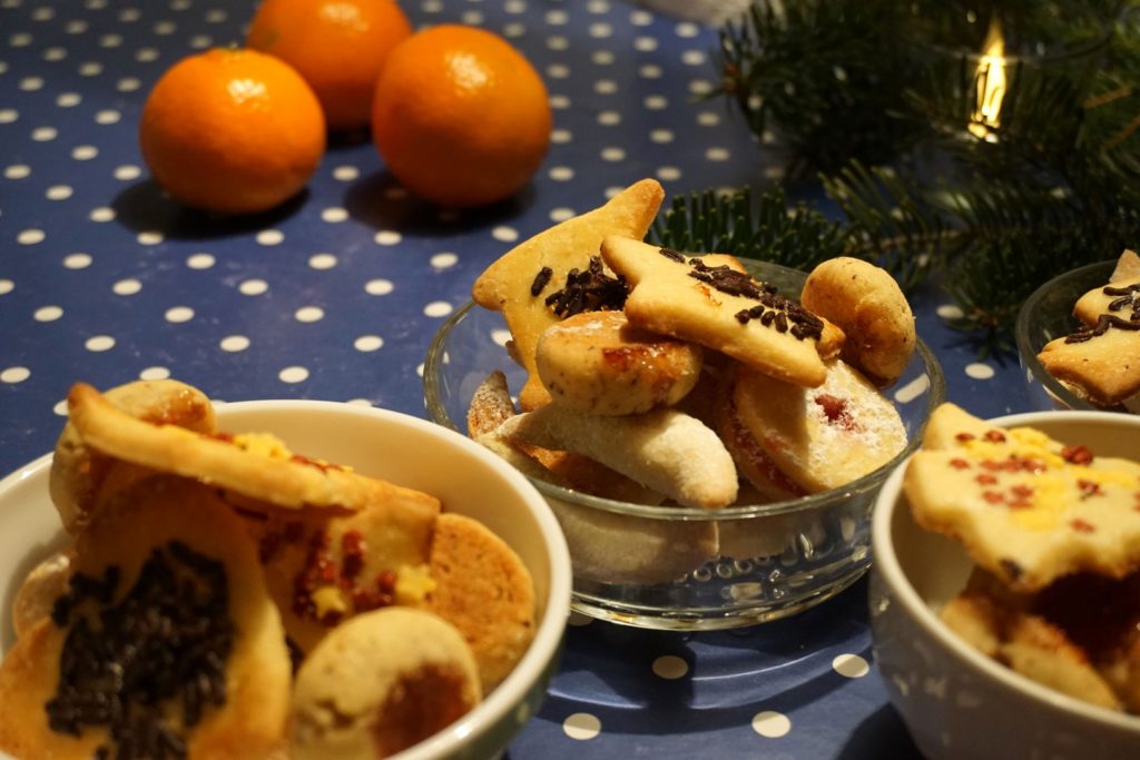 Selbst gebackene Kekse von Doris. Das Bild zeigt drei kleine Schüsseln mit selbst gebackenen Keksen. Im Hintergrund etwas Tannengrün und drei knallig, orangene Mandarinen.