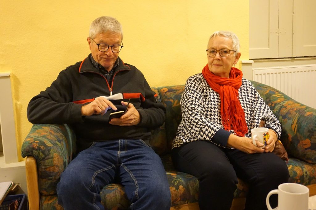 Calle und Renate sitzen auf einem Sofa in einem der Räume. Calle recherchiert gerade etwas am Handy.