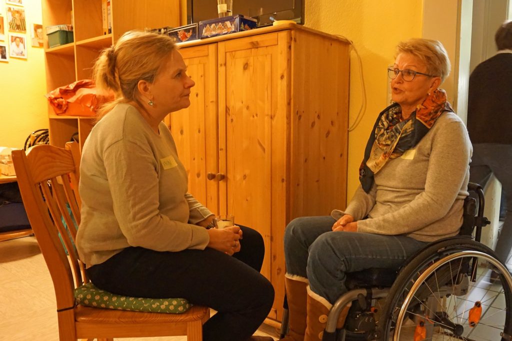 Auf dem Bild zu sehen sind Karin (auf einem Stuhl sitzend) und Rita (im Rollstuhl). Die beiden arbeiten im Rahmen des Checker-Teams zusammen.
