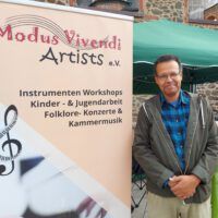 Ein Herr steht neben dem Banner von Modus Vivendi Artist