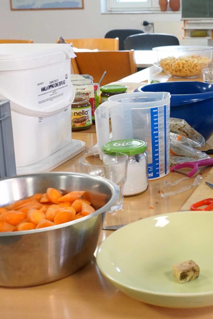 Auf dem Tisch stehen geschnittene Karotten, ein Meßbecher, ein Teller