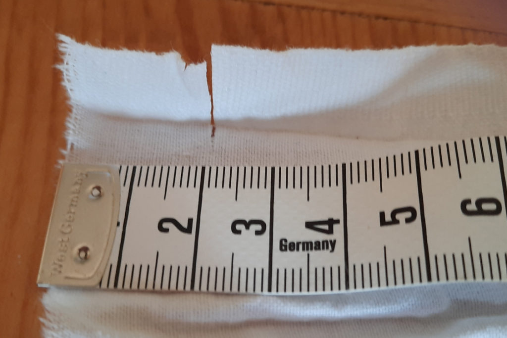 Baumwollstoff abmessen und bei 2 cm einreißen. Das Bild zeigt weißen Stoff mit einem Lineal darauf.