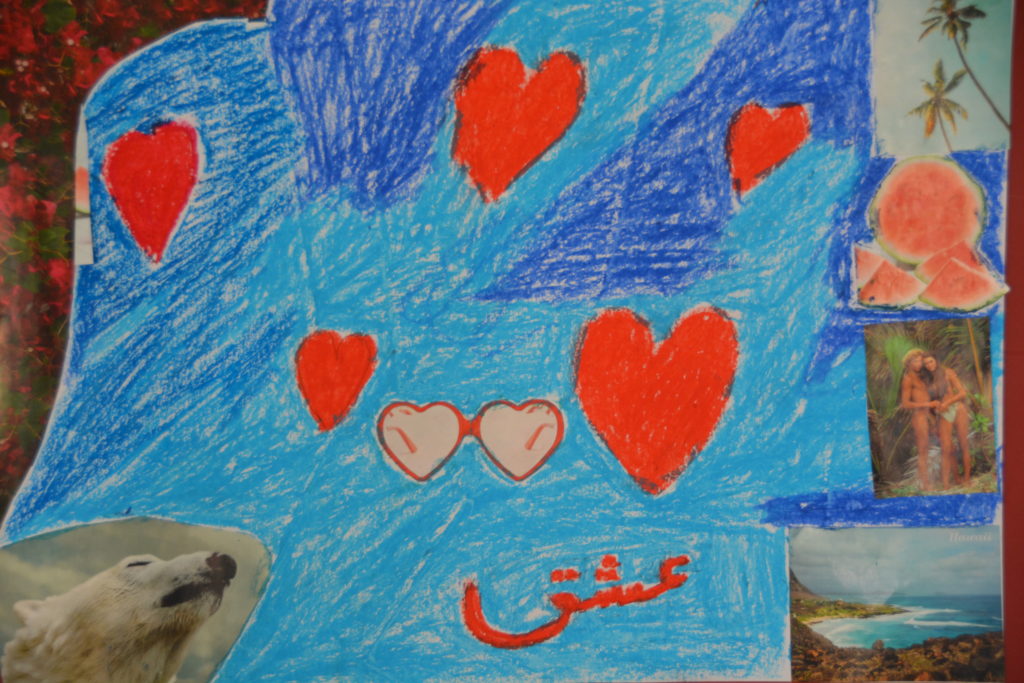 Ein in hellblau und blau gehaltener Hintergrund, auf dem viele rote Herzen gemalt sind. In arabisch das Wort Liebe. Rund herum befinden sich Bilder aus Zeitungen ausgeschnitten. Zum Beispiel ein Eisbär oder ein Pärchen.