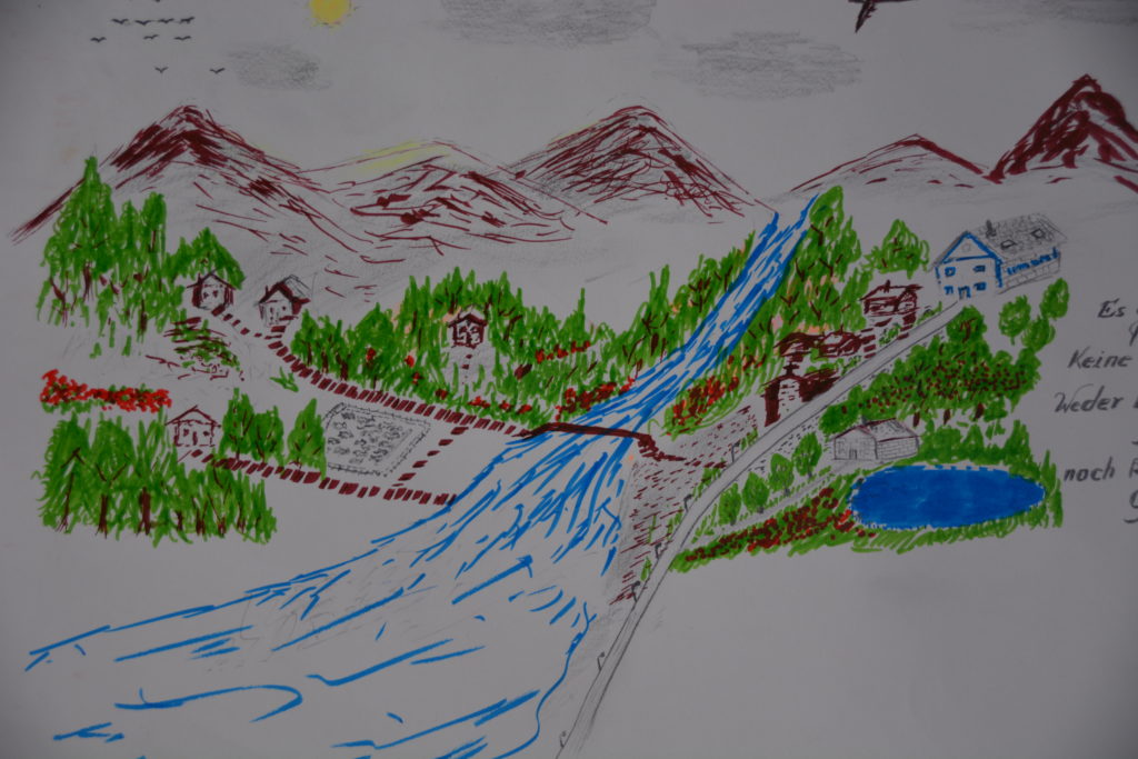 Das Bild zeigt eine Landschaft mit einem Fluß, im Hintergrund hohe, braun gestaltete Berge. Über den Fluss führt eine Brücke, die die auf beiden Seiten vorhandenen, kleinen Häuser verbindet.