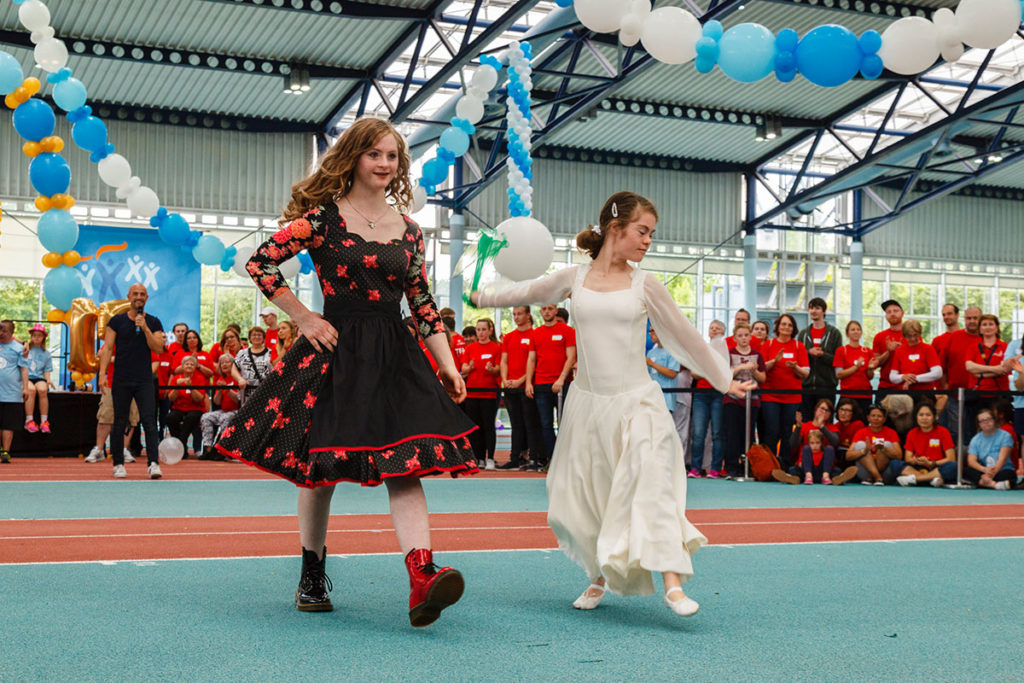 Das Bild zeigt zwei junge Mädchen, die in einem schicken Kleid über einen Laufsteg stolzieren - Modenschau als Rahmenprogramm.