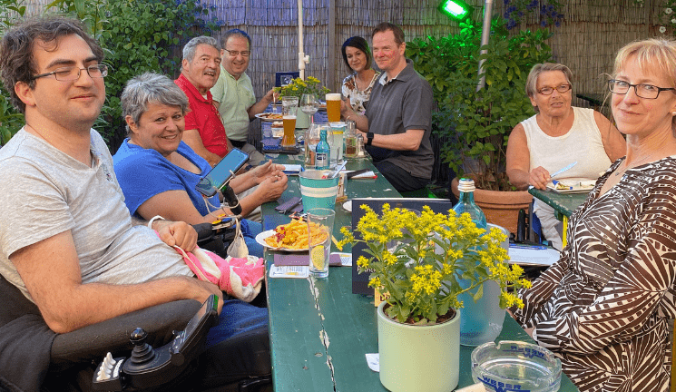 Checker Team sitzt an einer gemeinsam an einer Bierzeltgarnitur mit Essen, Blumen und Trinken auf dem Tisch. Alle lachen in die Kamera.