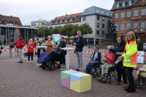 2022: Mehrere Personen, darunter drei in Rollstuühlen, sind auf dem Marktplatz. Sie sind gerade mit dem Stegreiftheater fertig.