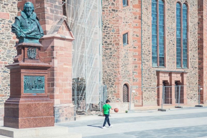 Vor der Wallonisch-Niederländischen Kirche spielt ein Junge mit grünem T-Shirt mit einem Basketball. Dieser scheint wie schwerelos mit seiner Hand verbunden.