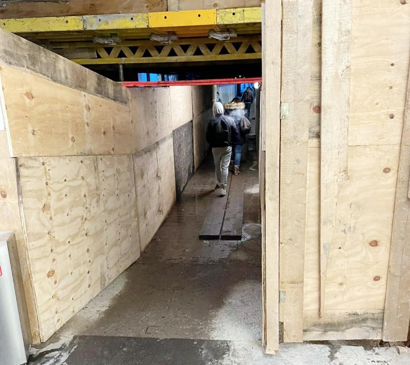 In der Unterführung am Hanauer Bahnhof befindet sich eine Baustelle. Die Wände sind mit einer Holzkonstruktion eingefasst, es öffnet sich ein enger schräger Gang. Mitten auf dem Durchweg liegen 2 Bretter über einer rießigen Pfütze.