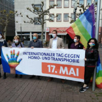 Sechs Menschen halten in der Hanauer Innenstadt einen großen Schriftzug, auf dem in großen Buchstaben der 17. Mai als Internationaler Gedenktag gegen Homo- und Transphobie (IDAHOBIT) geschrieben steht.