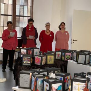 2025: Vier Frauen in roter Kleidung stehen hinter vielen Laternen. Diese Laternen wurden im Rahmen der Internationalen Wochen gegen Rassismus gebastelt und kreativ gestaltet.