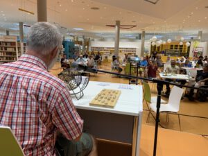 2022: Ein Mann sitzt vor Publikum im Kulturforum. Vor ihm steht die Binogtrommel.