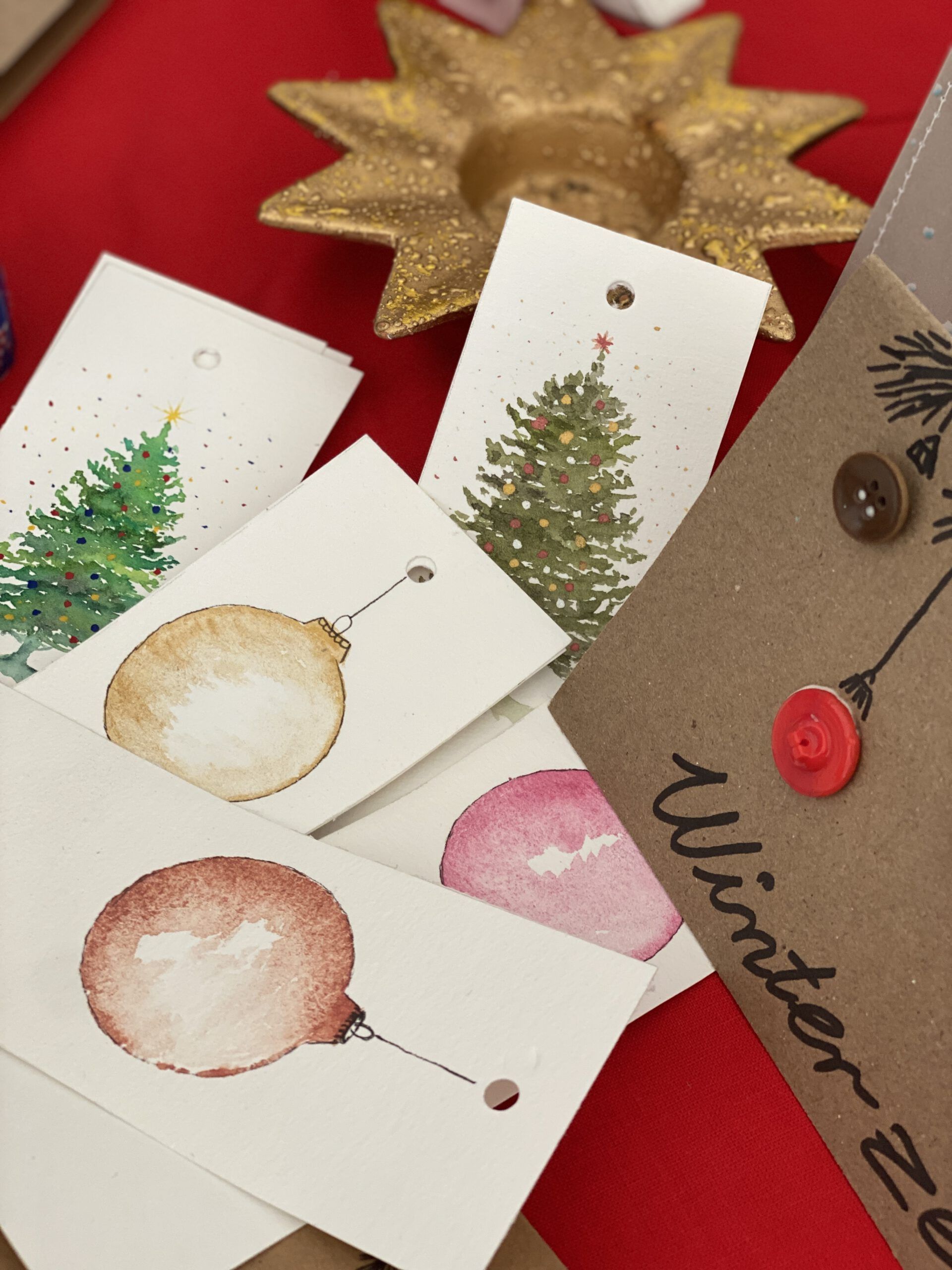 Geschenkkarten mit Christbaumkugeln und Weihnachtsbäumen auf einer roten Tischdecke