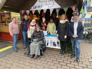 2022: Mehrere Personen stehen vor bzw. in einer Weihnachtsmarkthütte auf dem Hanauer Weihnachtsmarkt. Die Hütte ist mit Bannern von Menschen in Hanau geschmückt.