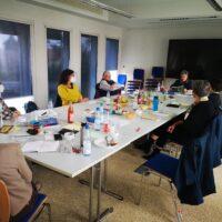 Es ist der Raum mit den Teilnehmern des Schreib-Workshops zusehen die um einen Tisch herum sitzen
