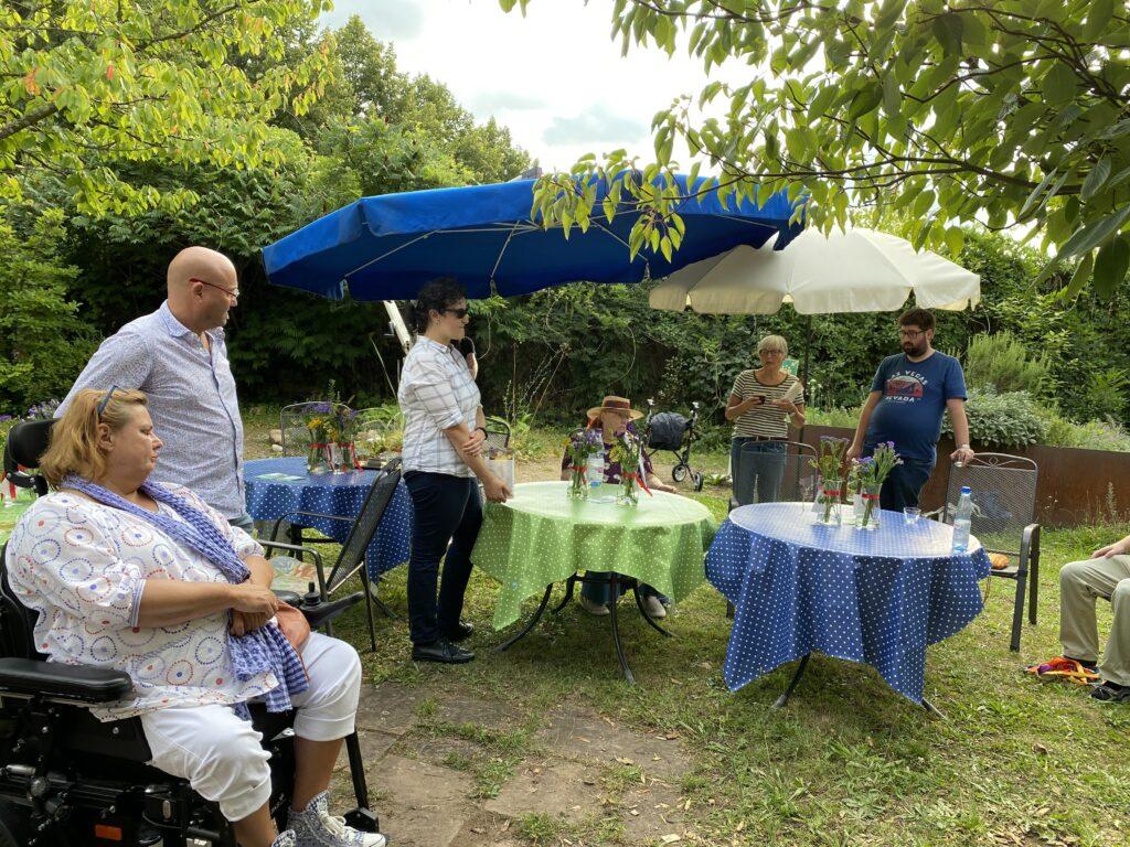 Gäste des Sommerfestes stehen um Tische herum und sprechen miteinander.
