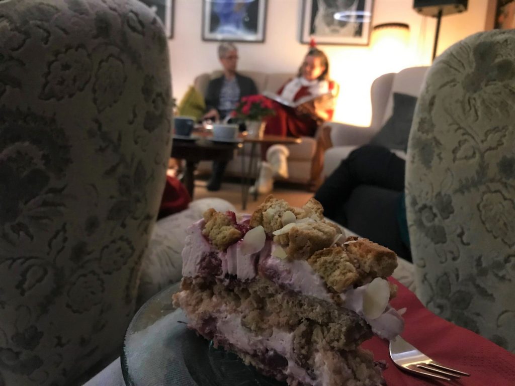 Eine leckere Torte mit Kischen und Quark ist fokussiert. Im Hintergrund sieht man durch zwei Sessel hindurch Bea und Patricia auf der Bühne.