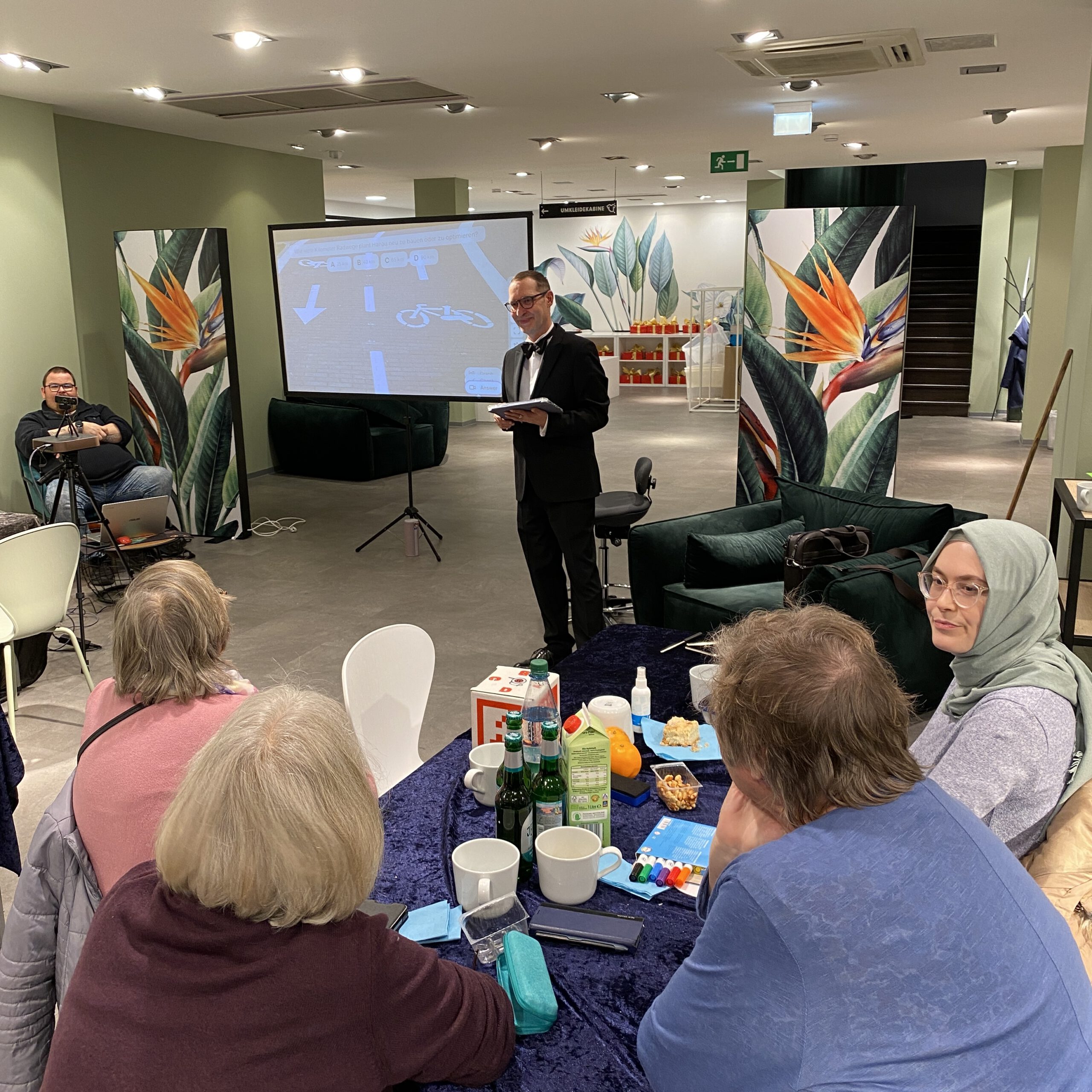 Thorsten im schwarzen Anzug steht als Moderator vor der Gruppe