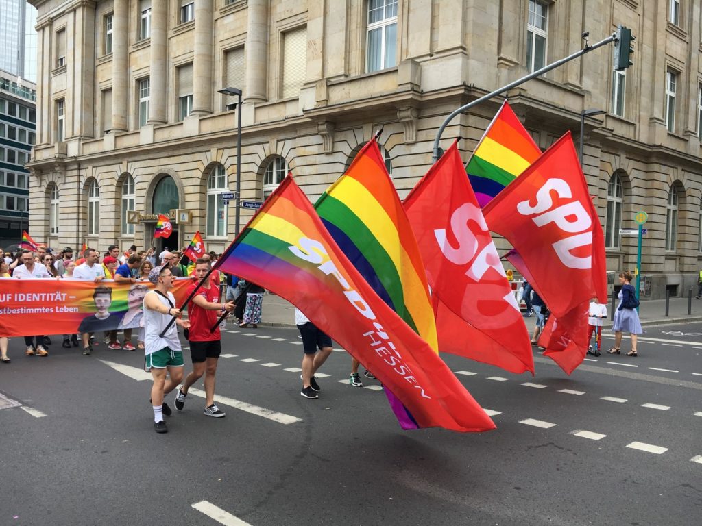 Das Bild zeigt die Gruppe der SPD. Vorweg sechs Menschen, die jeweils eine Regenbogen-Fahne und eine SPD-Farbe im Wechsel halten.