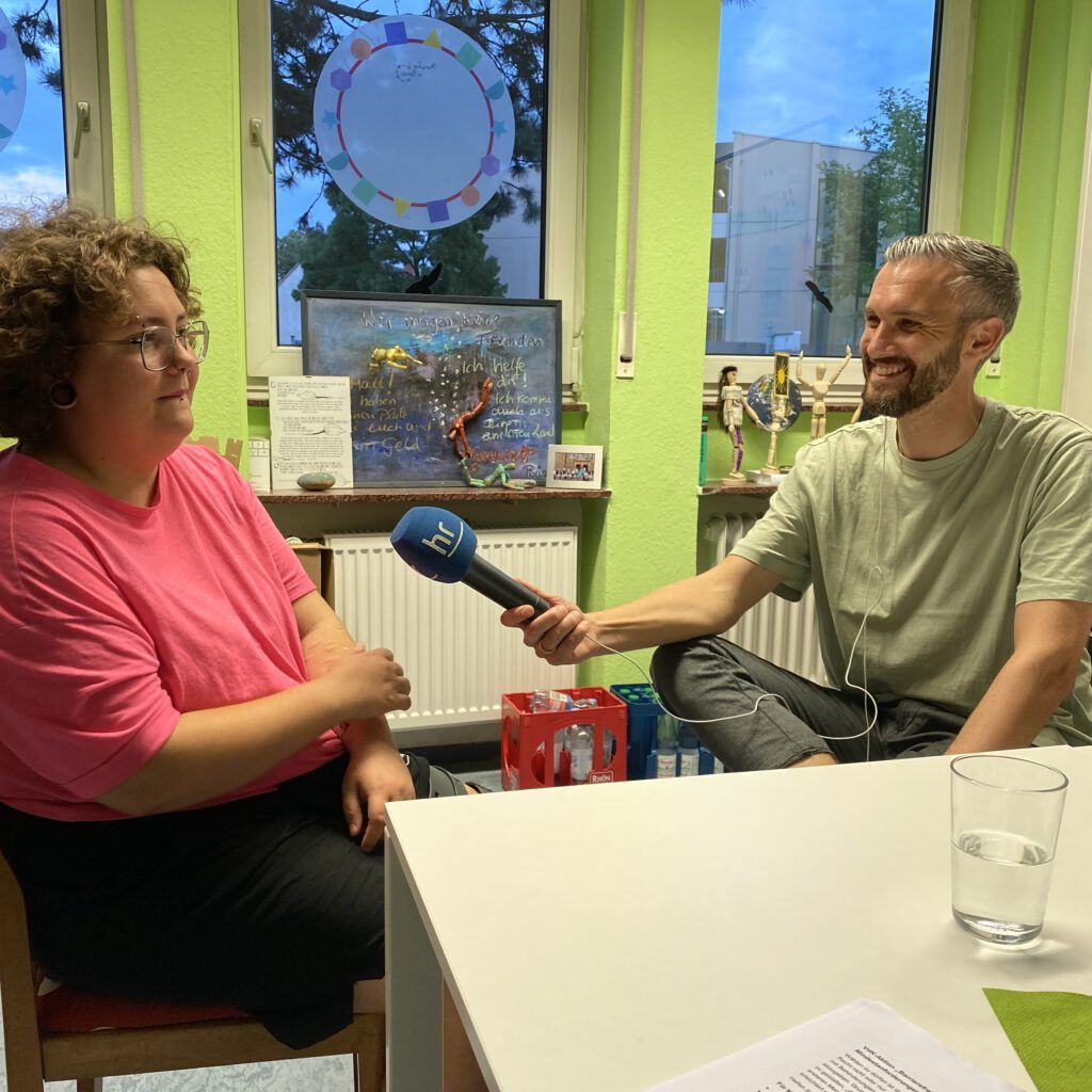 Kathi, eine junge Frau mit gelocktem Haar und pinkem Oberteil, wird von Heiko interviewt.