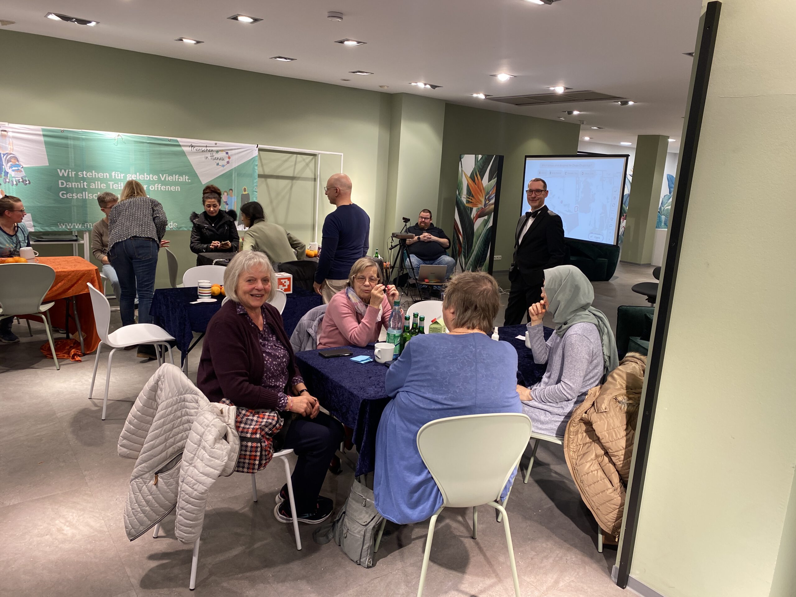 Alle sitzen um ihre Tische und einige lache nin die Kamera