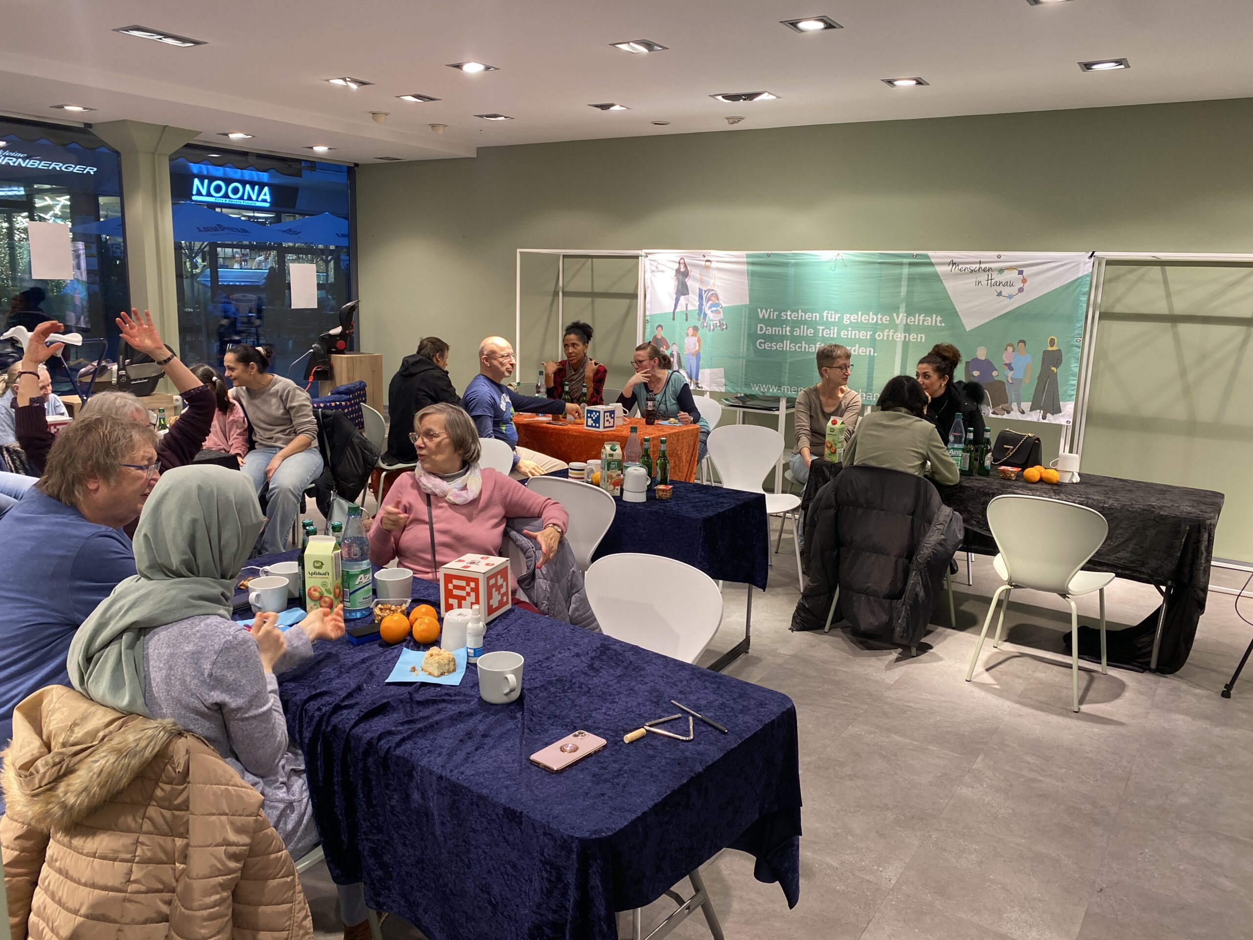 Der ganze Raum ist zu sehen und die Leute sitzen an mehreren bunt gedeckten Tischen.