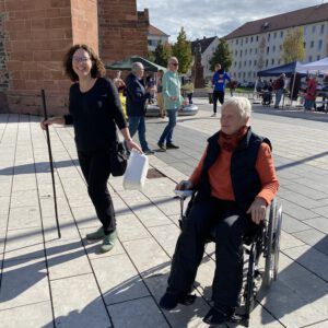 Eine Frau im Rollstuhl und eine Frau mit Material für den Parcours lachen.