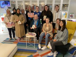 2023: Internationale Wochen gegen Rassismus: Viele Frauen sitzen oder stehen vor einem Regal mit Puppen, die MiH künstlerisch bearbeitet hat. Das Foto wurde bei IKEA aufgenommen. Dort gab es auch eine Ausstellung der Puppen.
