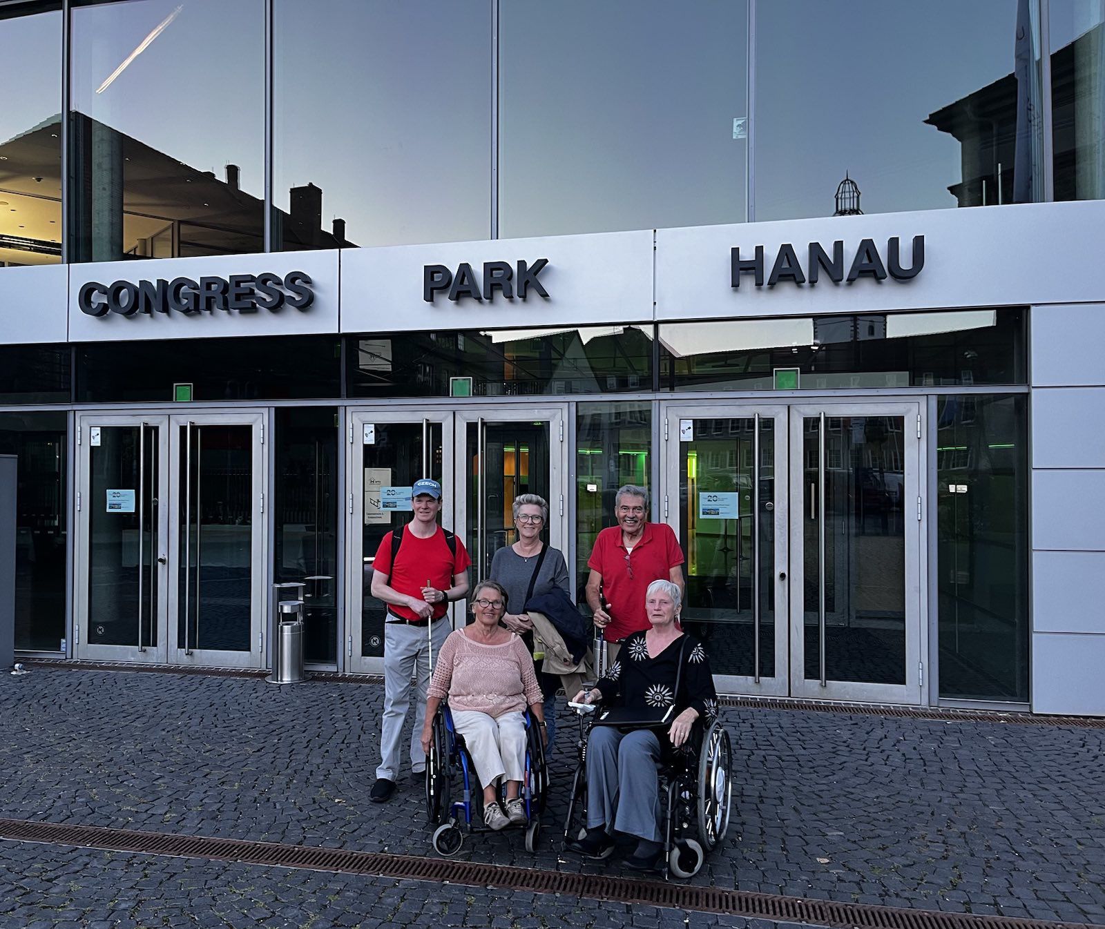 Gruppe, 2 Rollstuhlfahrer und 3 Personen dahinter, steht zusammen vor dem Eingang des CPH.