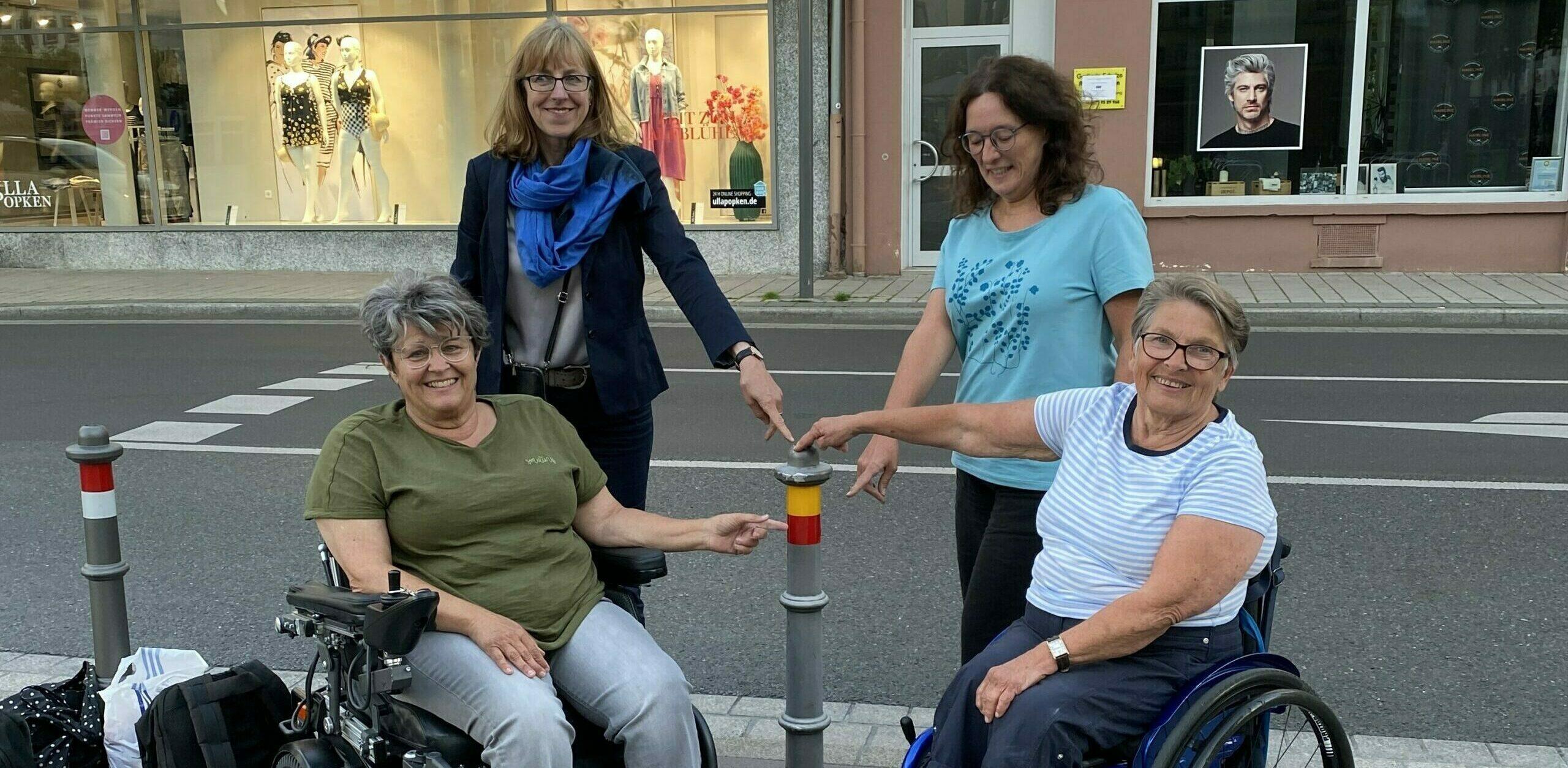2 Menschen mit und 2 ohne Rollstuhl zeigen auf einen Roller mit einem gelb-roten Kontraststreifen