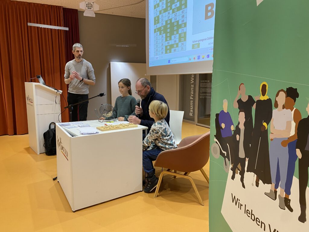 Ein grüner Menschen in Hanau Banner und Mensschen vor einer großen Leinwand im Kulturforum