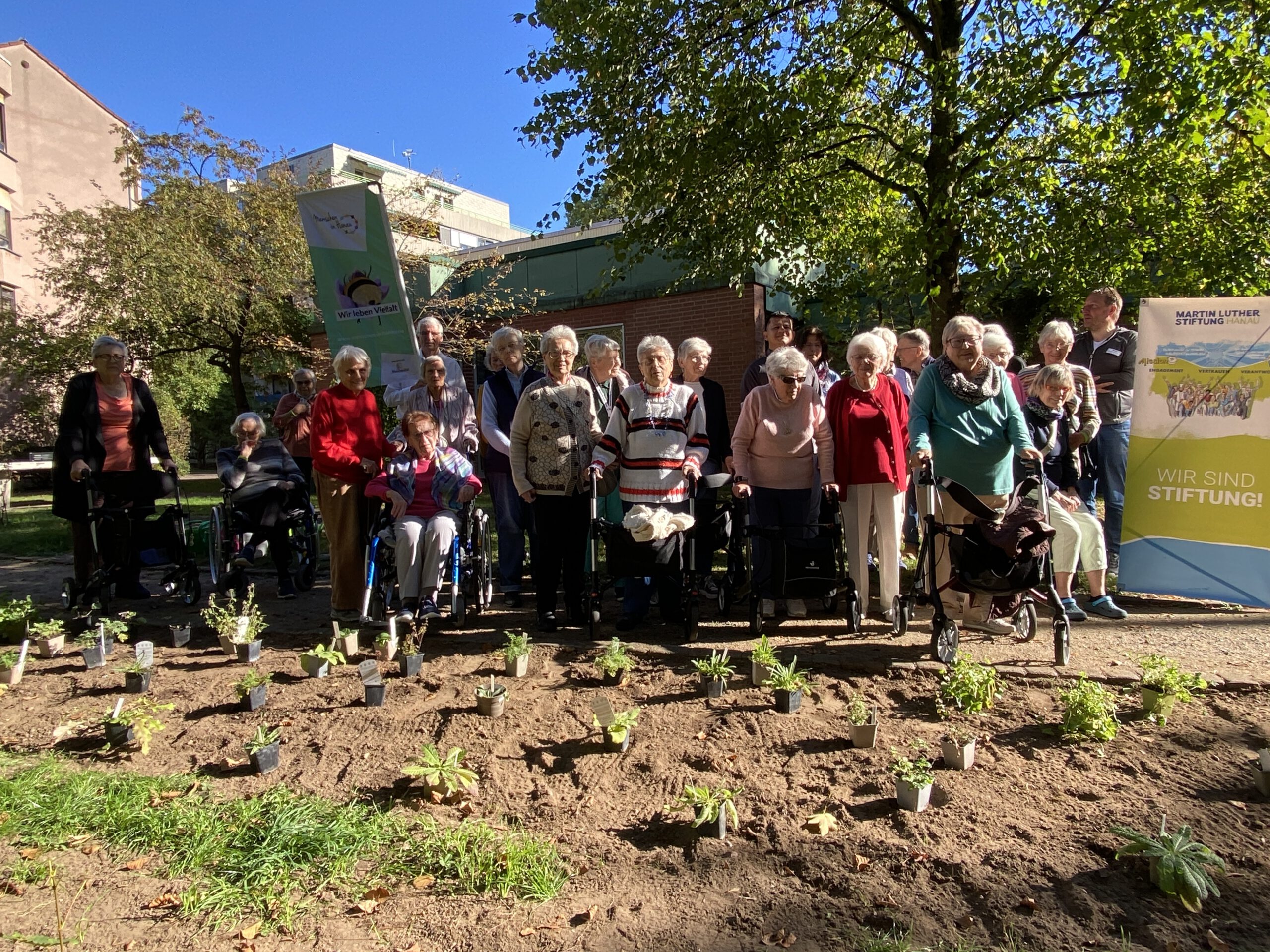 Gruppenfoto der Bewohner:innen und Helfer:innen hinter dem frisch bepflanzten Beet in der Sonne.