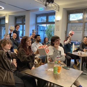 2025: Mehrere Personen beim Pub-Quiz. Sie halten Würfel aus Pappe mit aufgedruckten QR-Codes hoch.