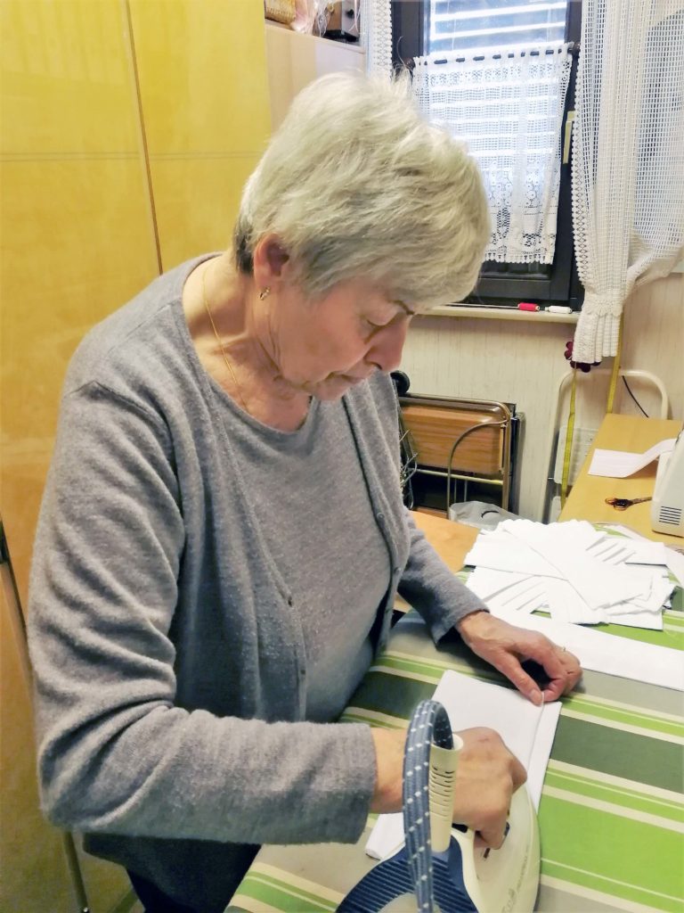 Eine Frau bügelt Masken auf einem grün-gestreiften Bügelbrett.