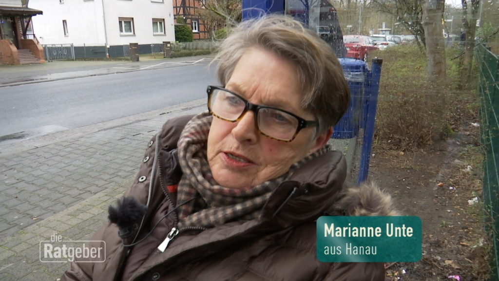 Marianne auf dem Weg nach Hanau. Sie sitzt in ihrem Rollstuhl und wartet an einer Bushaltestelle auf den Bus.