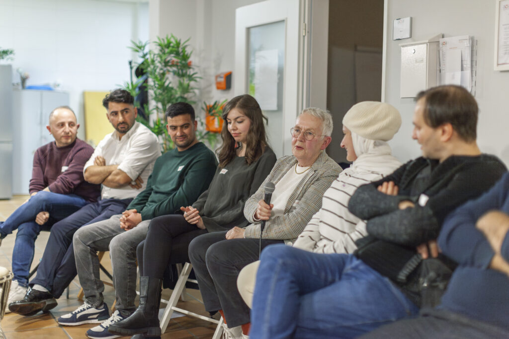 Mehrere Menschen sitzen in einer Reihe und sind am Mikrofon